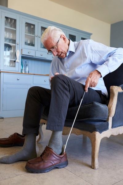 elderly man using a shoe horn to put shoe on
