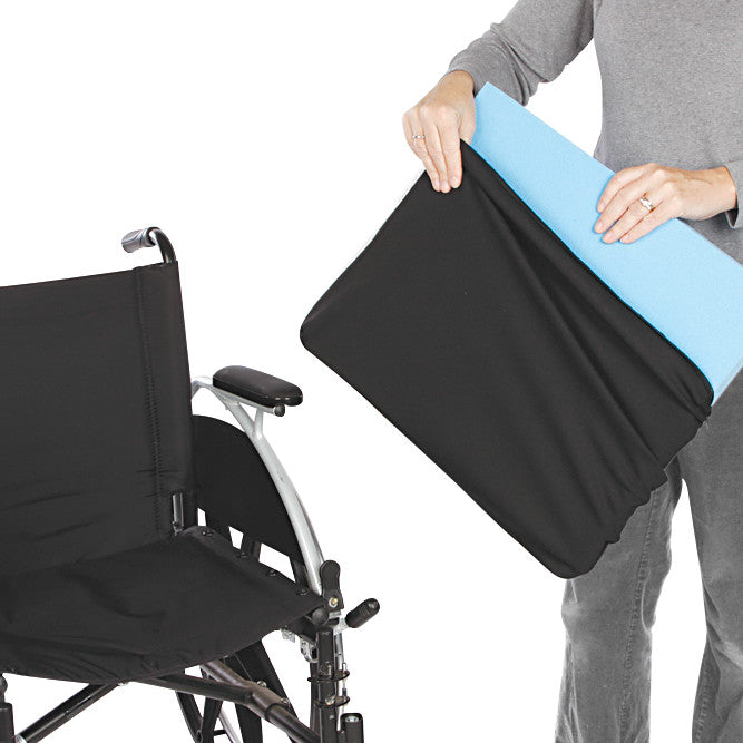 A person holds an AliMed Replacement Wheelchair Cushion Cover with a blue foam cushion, next to a wheelchair.