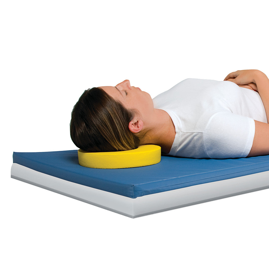 A person lies on their back using the AliMed Protecta-Coat Head Donut, a yellow foam ring, for head support on a blue mat.