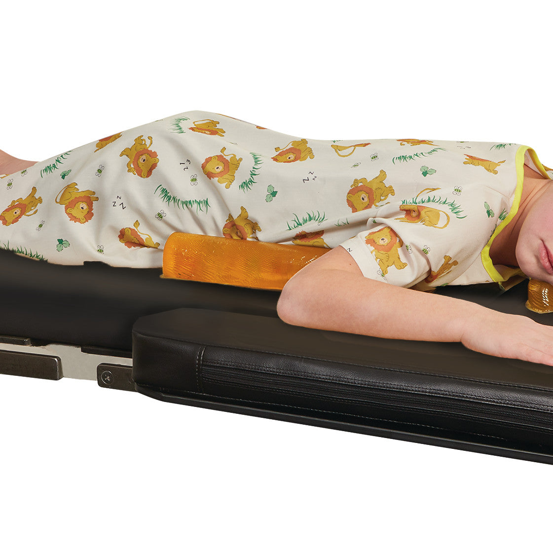 A child is lying face down on a medical table, dressed in lion-print attire, supported by an AliMed AliGel Chest Roll under the torso.