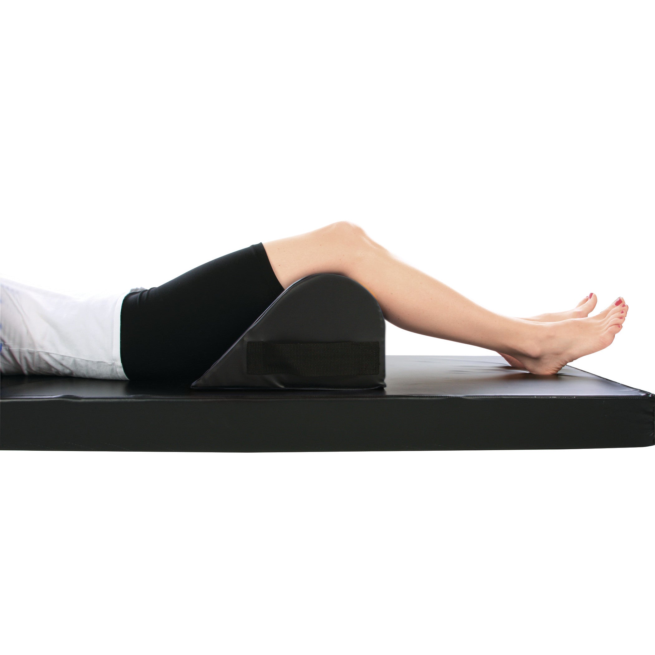 A person reclines on a mat using the AliMed Vinyl-Covered Standard Knee Bolster to support their knees, elevating the legs.