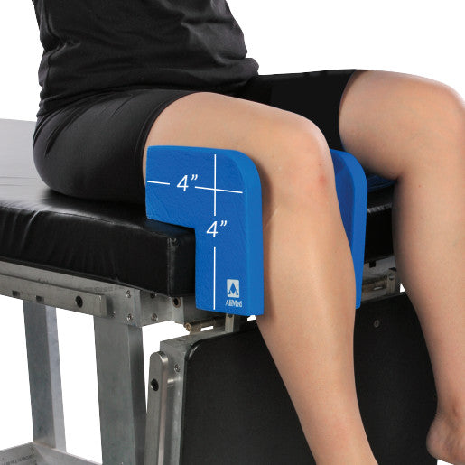 A person uses the AliMed Vinyl-Coated Well-Leg Holder to support their leg, with blue foam padding marked as 4"x4".