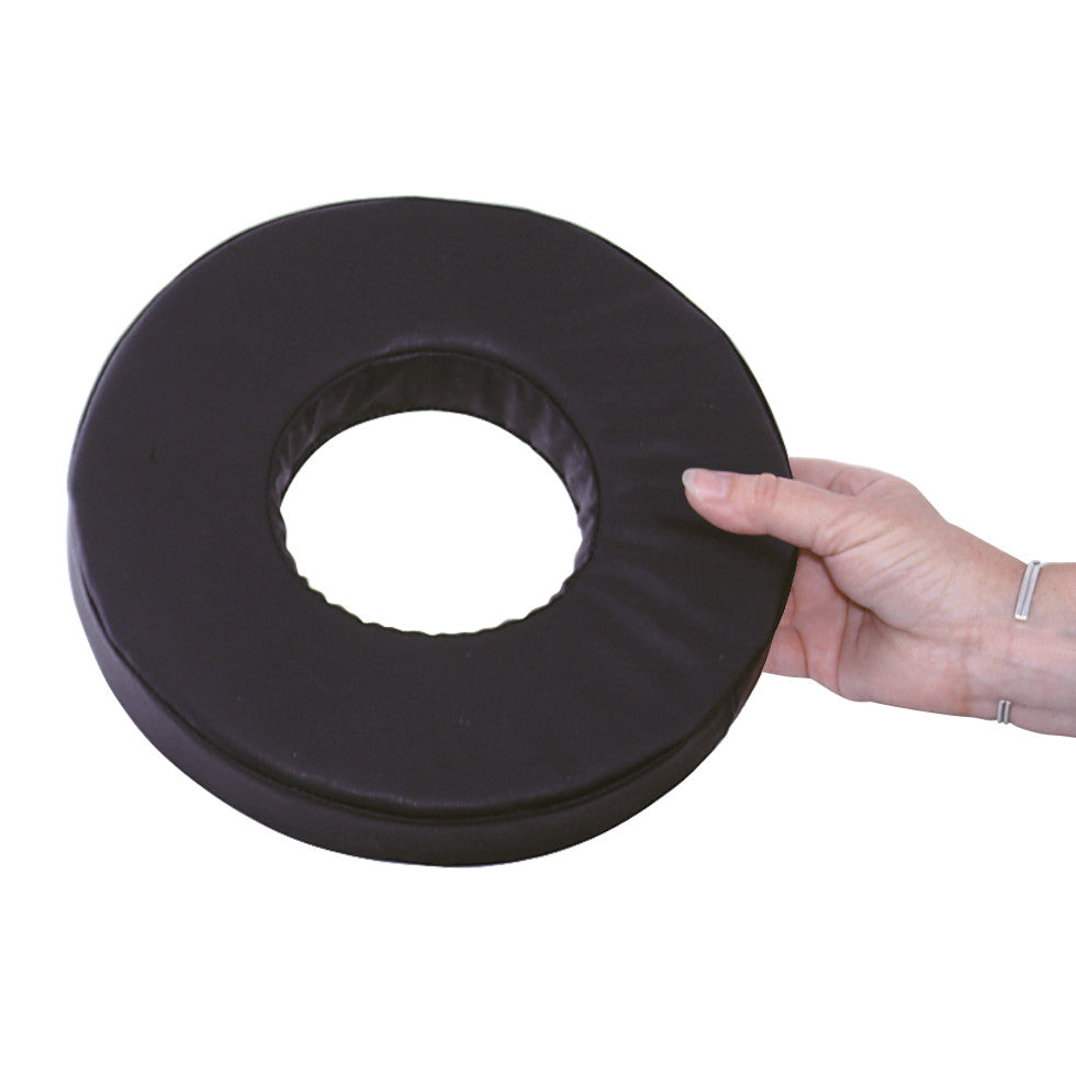 A hand holds the AliMed Conductive Black Vinyl-Covered Head Donut, a round cushion with a center hole, used for medical purposes.