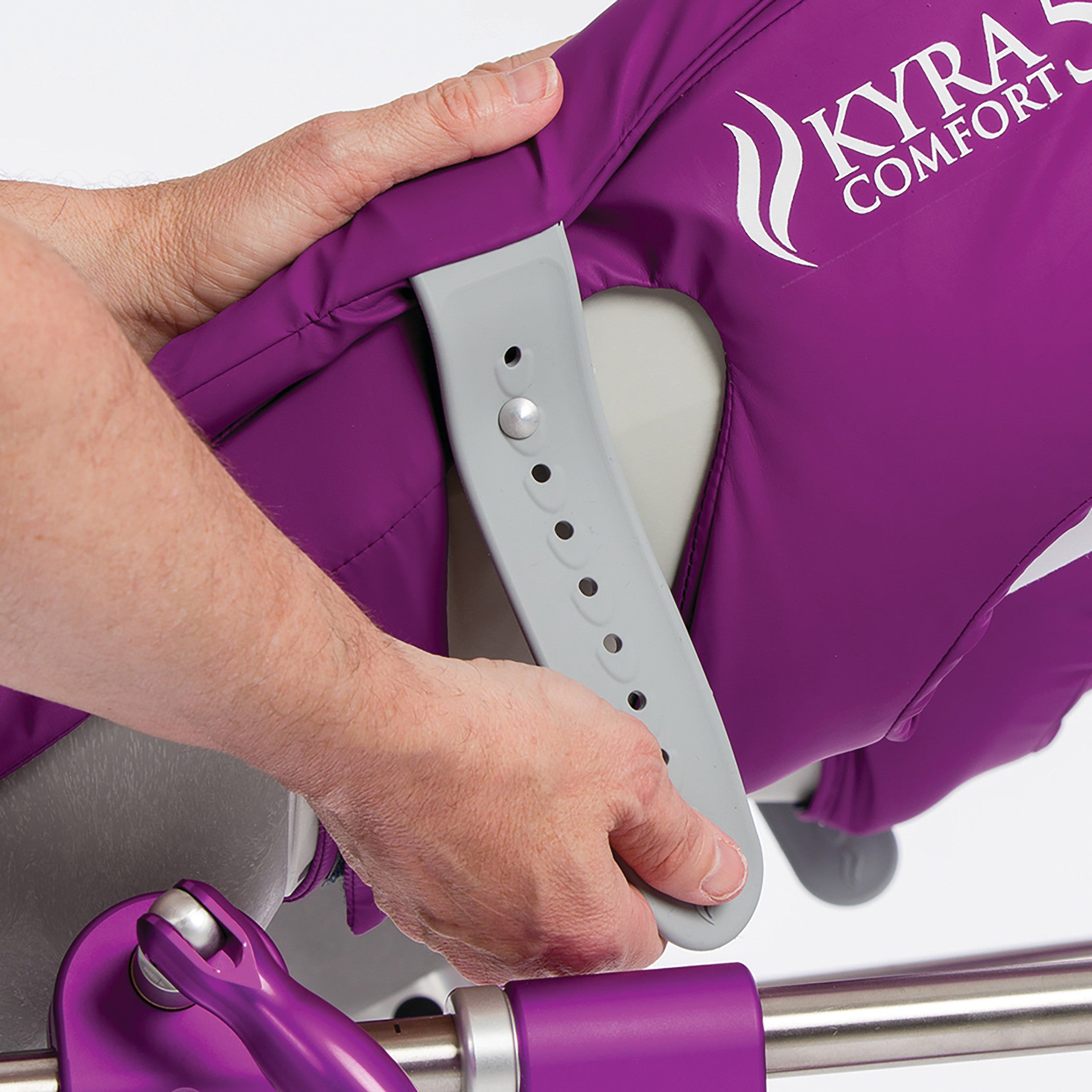 Hands adjusting a KYRA Comfort 800 Lithotomy Stirrup, featuring a purple padding and adjustable grey support arm.