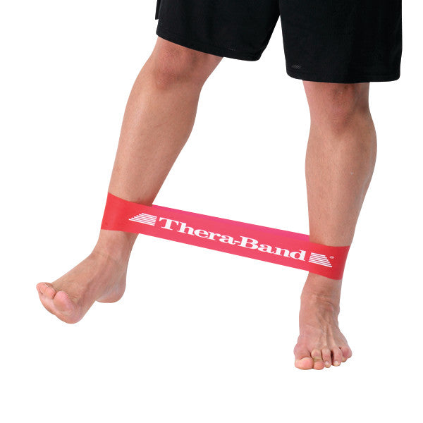 A red THERABAND Resistance Band Loop is wrapped around a person's lower legs, demonstrating a leg stretching exercise.