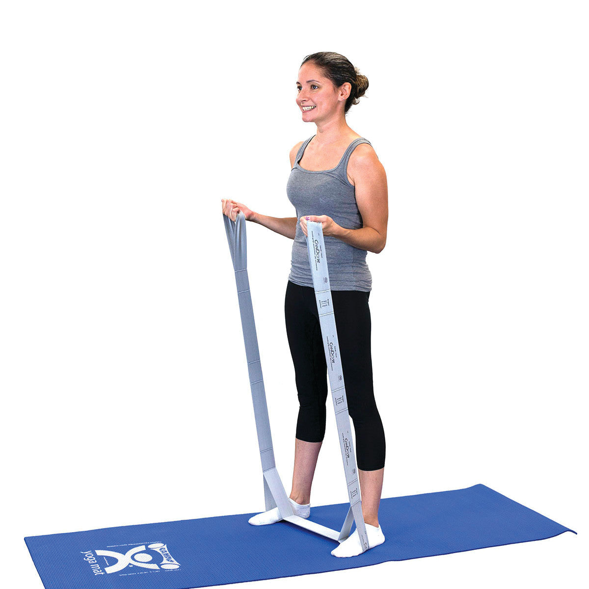 A person uses a CanDo Multi-Grip Exerciser on a blue mat, holding the resistance band, wearing a gray tank top and black capris.