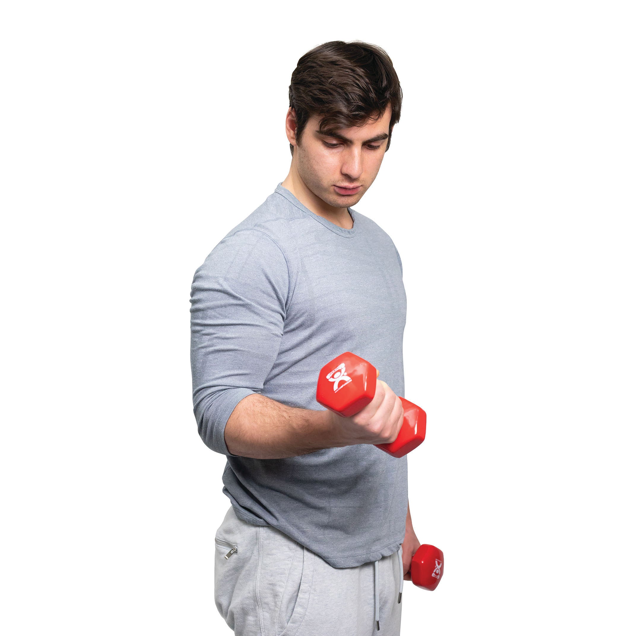 A person holds a red CanDo Vinyl-Coated Dumbbell in a bicep curl position, wearing a light gray shirt and sweatpants.
