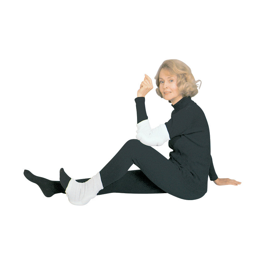 A woman wearing a black outfit with a SkiL-Care Heel/Elbow Protector on her elbow and heel, sitting against a white background.