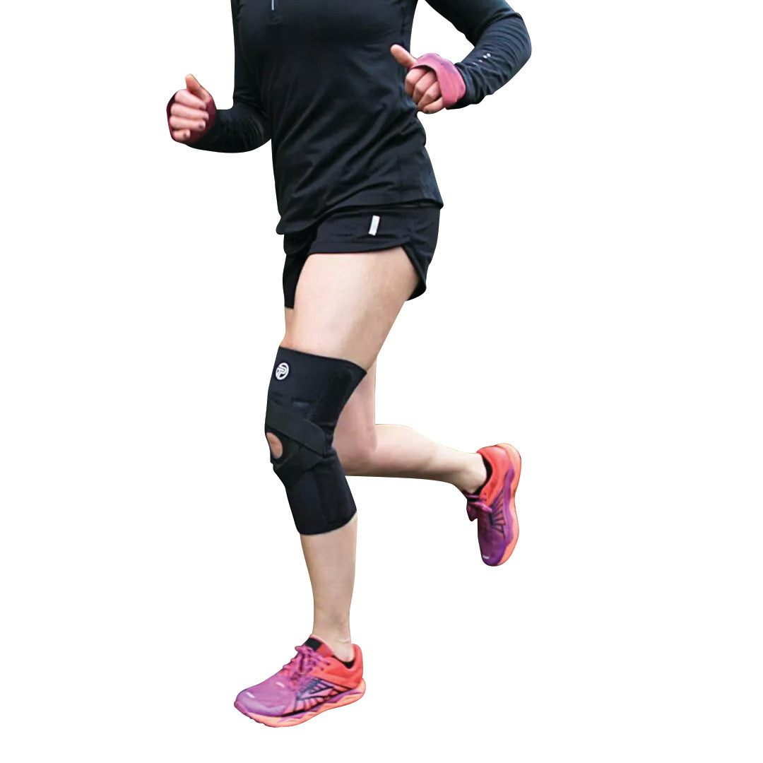 A person running, wearing a J-Lat Knee Support on their leg, dressed in black athletic wear with pink and orange running shoes.