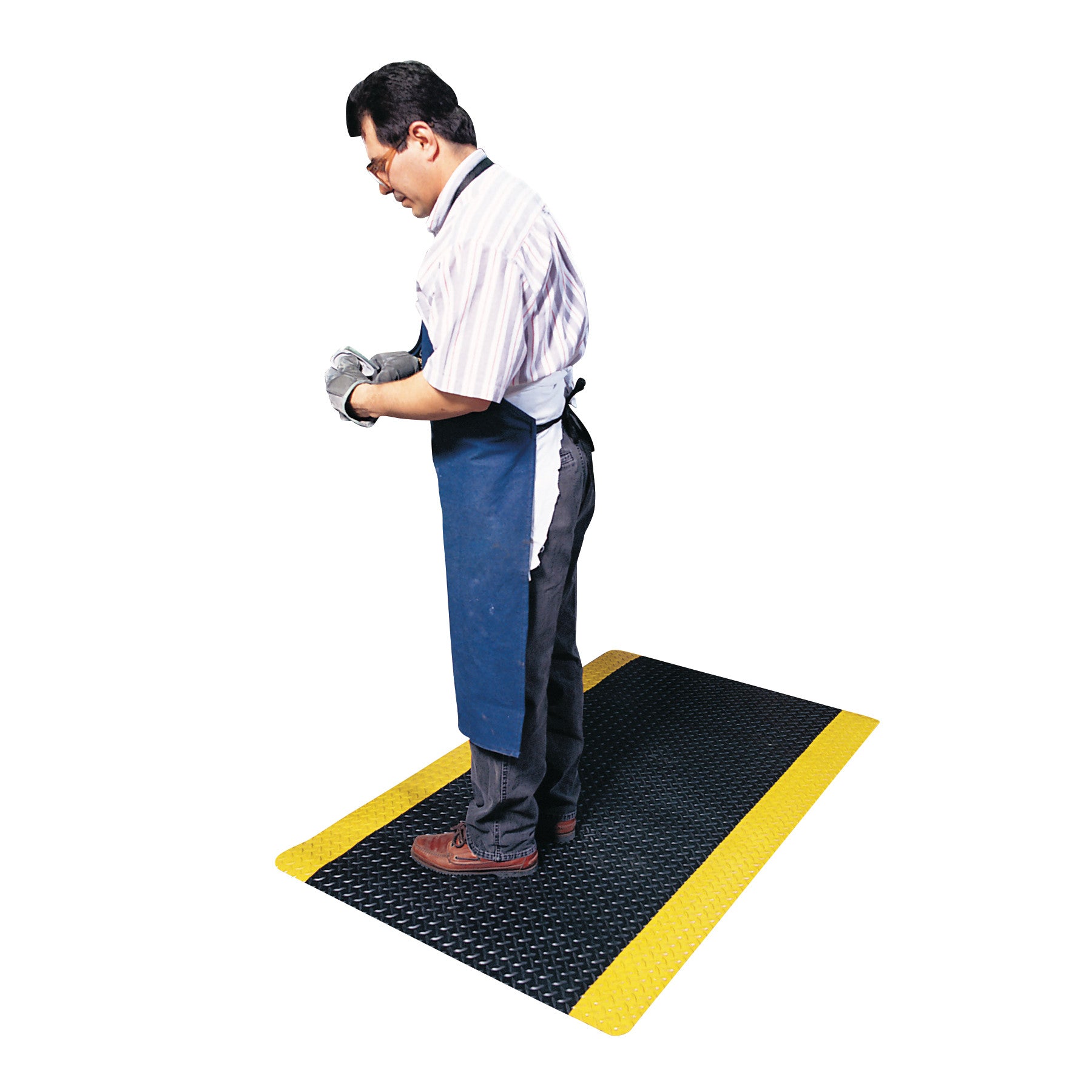 A man wearing an apron and gloves stands on a black Saddle Trax Anti-Fatigue Mat with yellow edges, providing ergonomic support.