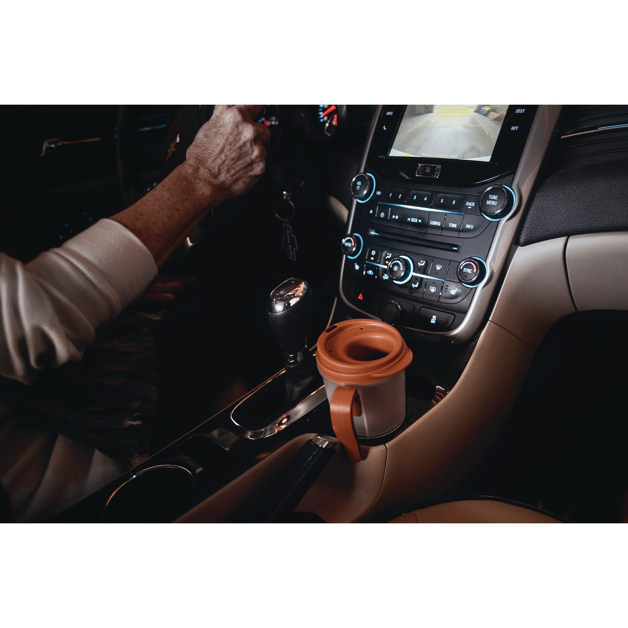 A Provale Cup with a brown lid sits in a car's cup holder. The car's dashboard and a person's arm are visible.