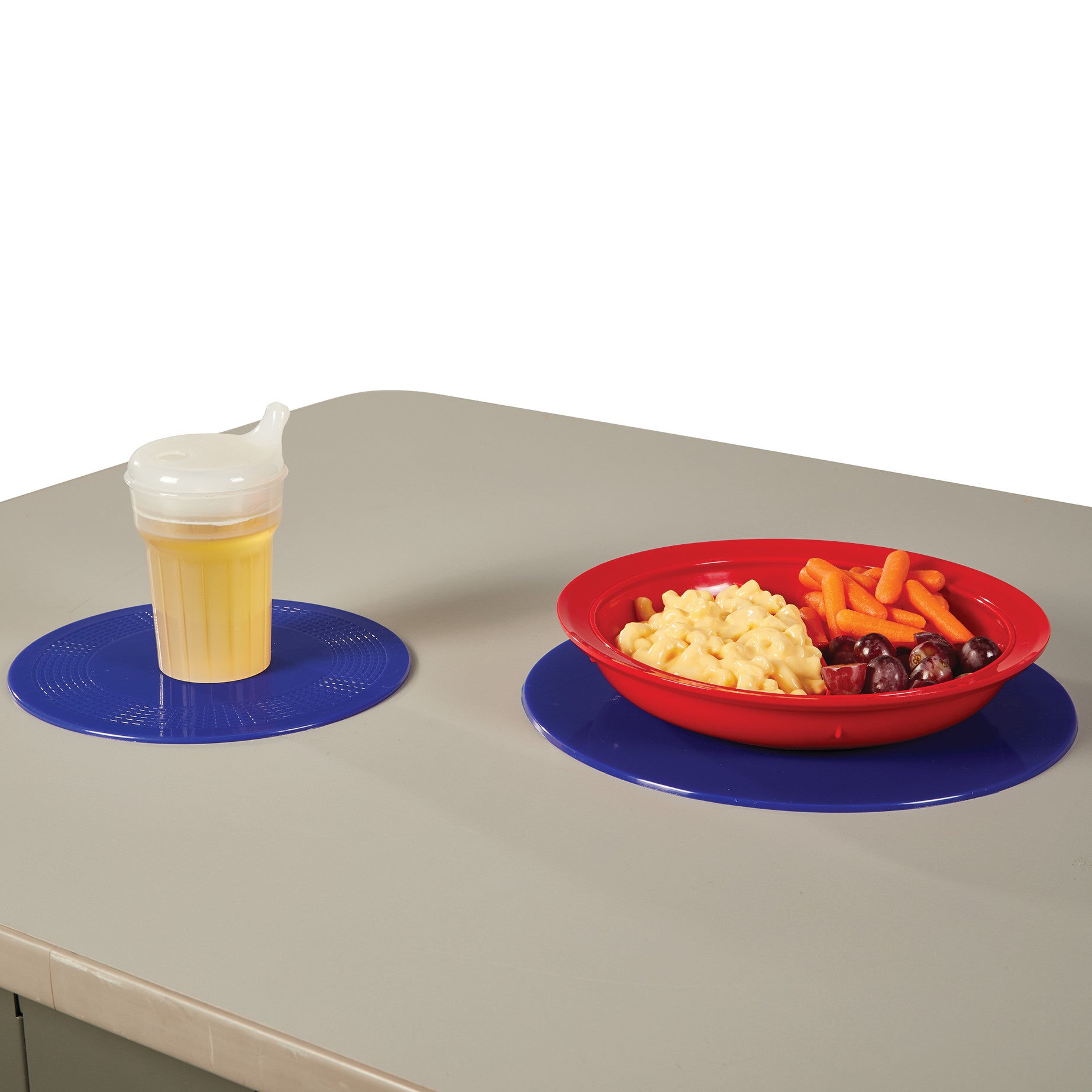 A sippy cup and red plate with food are on a gray table, each on a blue Dycem Nonslip Round Pad for stability.