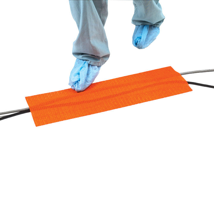 Person steps over cables covered by an orange SANDEL Trip-No-More Cord Alert, wearing blue shoe covers.
