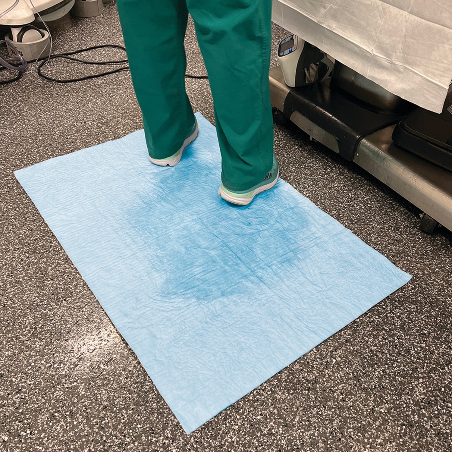 Person standing on a SpilfyterMED Blue Absorbent Mat for Heavy Spillage, placed on a speckled floor.