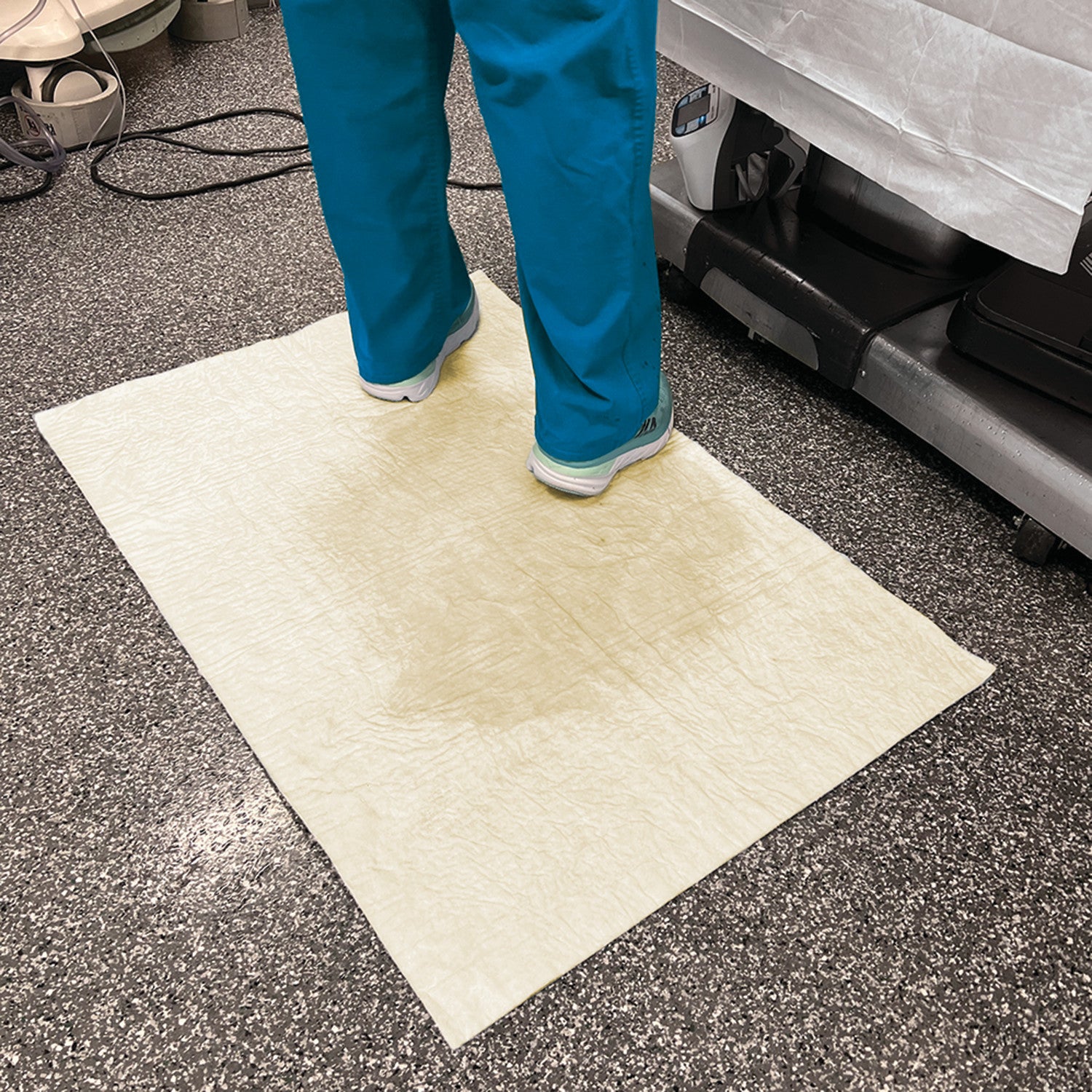 A person stands on a SpilfyterMED Yellow Absorbent Mat for Moderate Spillage in a medical setting, absorbing liquid on the floor.