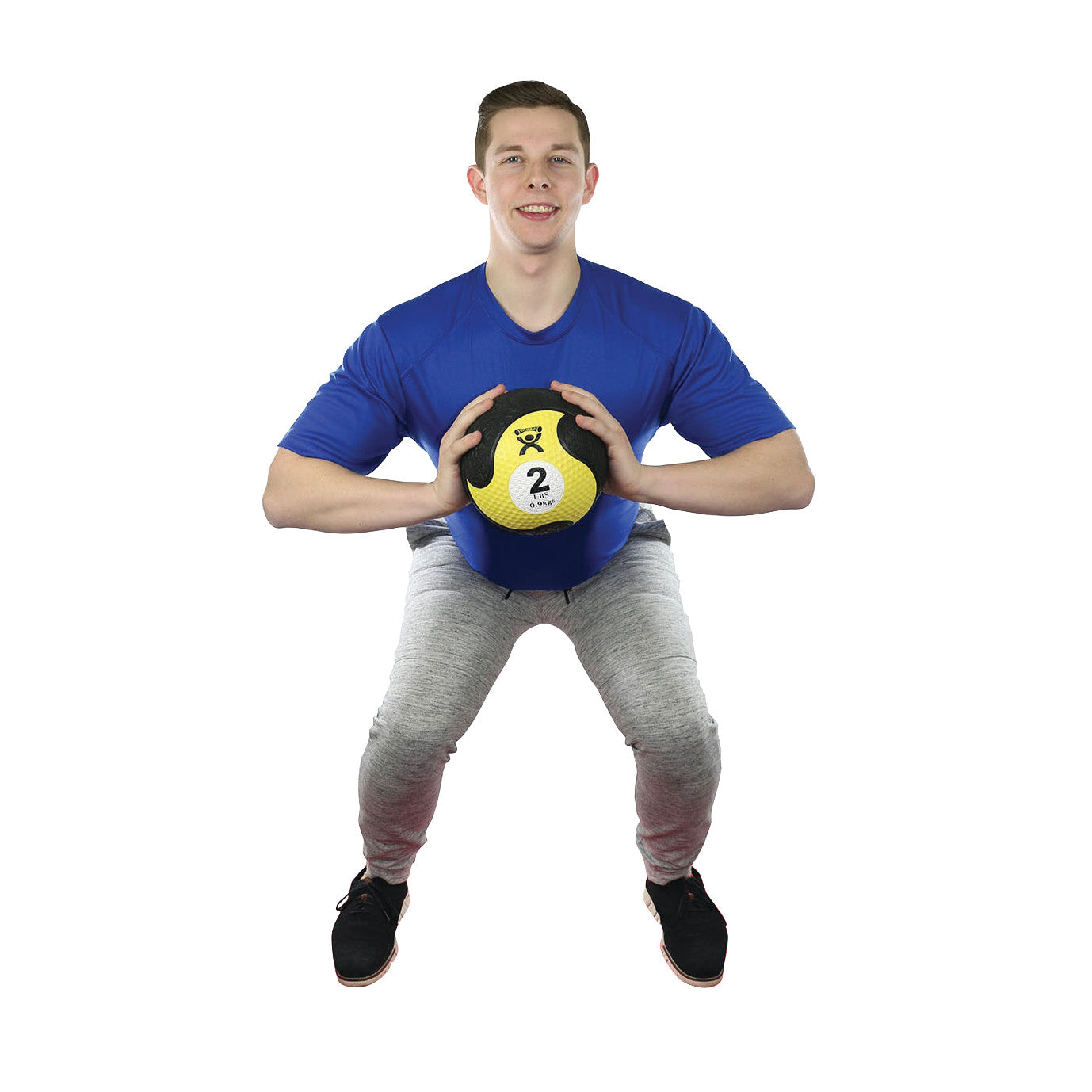 A man squats while holding a CanDo Rubber Medicine Ball, marked with "2" for kilograms, wearing a blue shirt and gray pants.