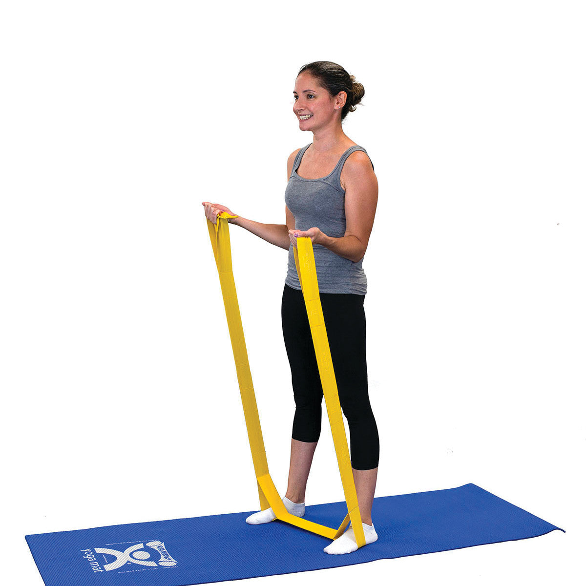 A person standing on a blue mat uses a yellow CanDo Multi-Grip Exerciser. They hold the band in both hands, arms bent slightly.