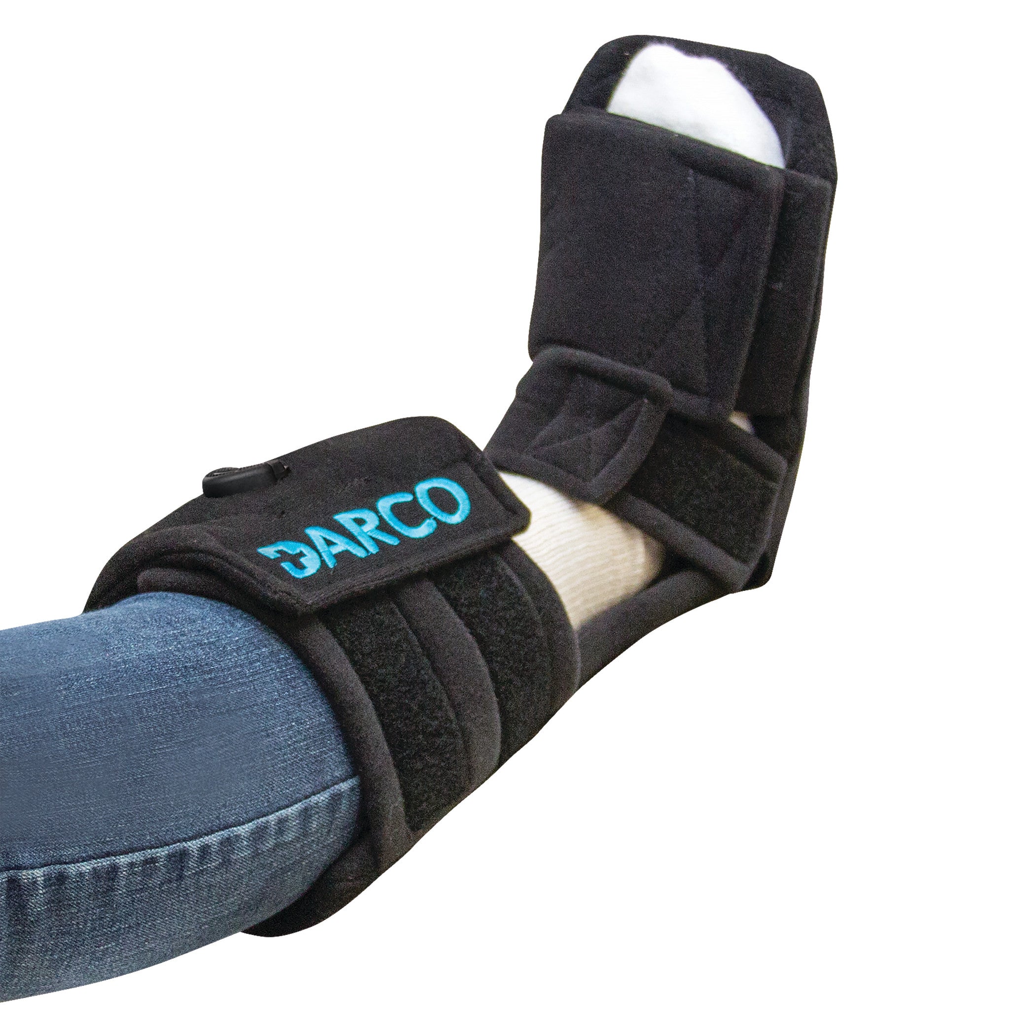 A person wears a DARCO Pneumatic Night Splint on their right foot, over a sock and jeans. The splint is black with blue lettering.