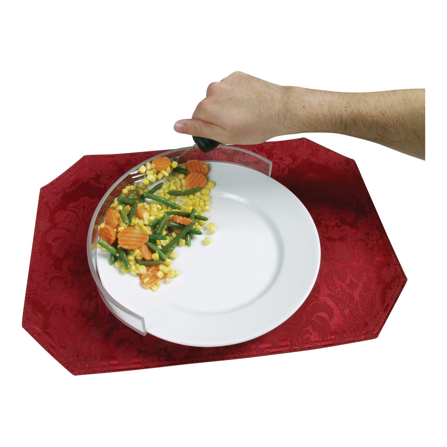 A hand uses a Therafin Plate Guard on a white plate with vegetables, placed on a red placemat.