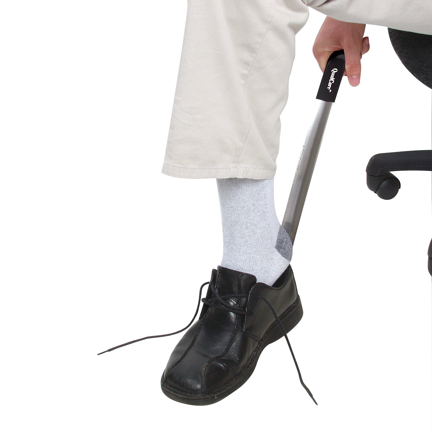 A person uses the Therafin Stainless Steel Shoehorn to put on a black shoe while sitting, wearing light-colored pants and gray socks.