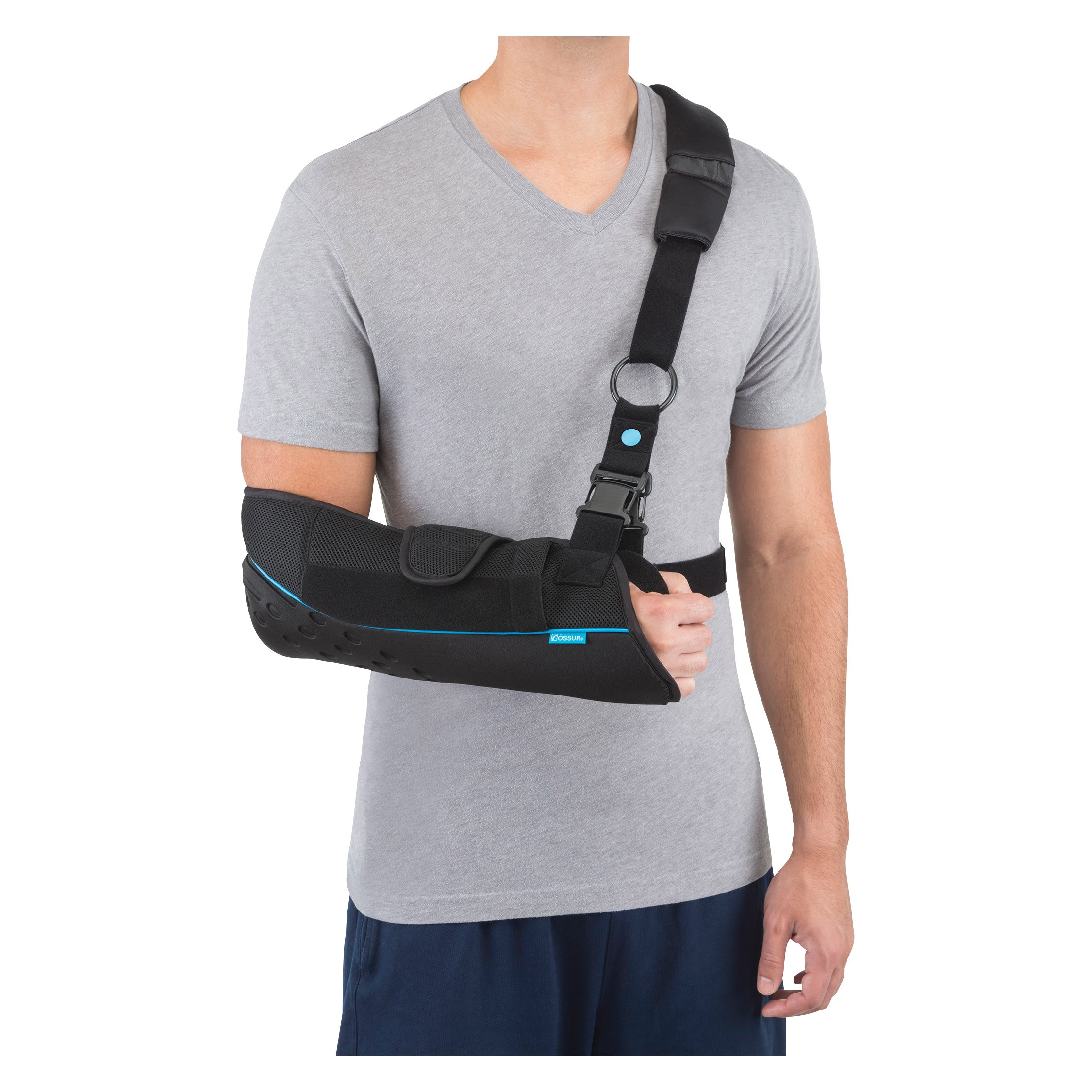 A person wears an Ossur Formfit Shoulder Brace, featuring a black arm sling with a padded shoulder strap, over a gray T-shirt.