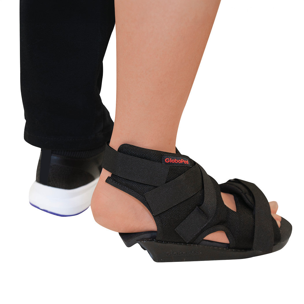 A person wearing a Bauerfeind GloboPed Heel Relief Orthosis, a black medical shoe designed to offload pressure from the heel.