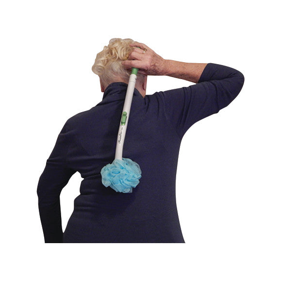 An elderly person uses a FreedomWand tool with a blue bath sponge to clean their back while wearing a navy long-sleeve shirt.