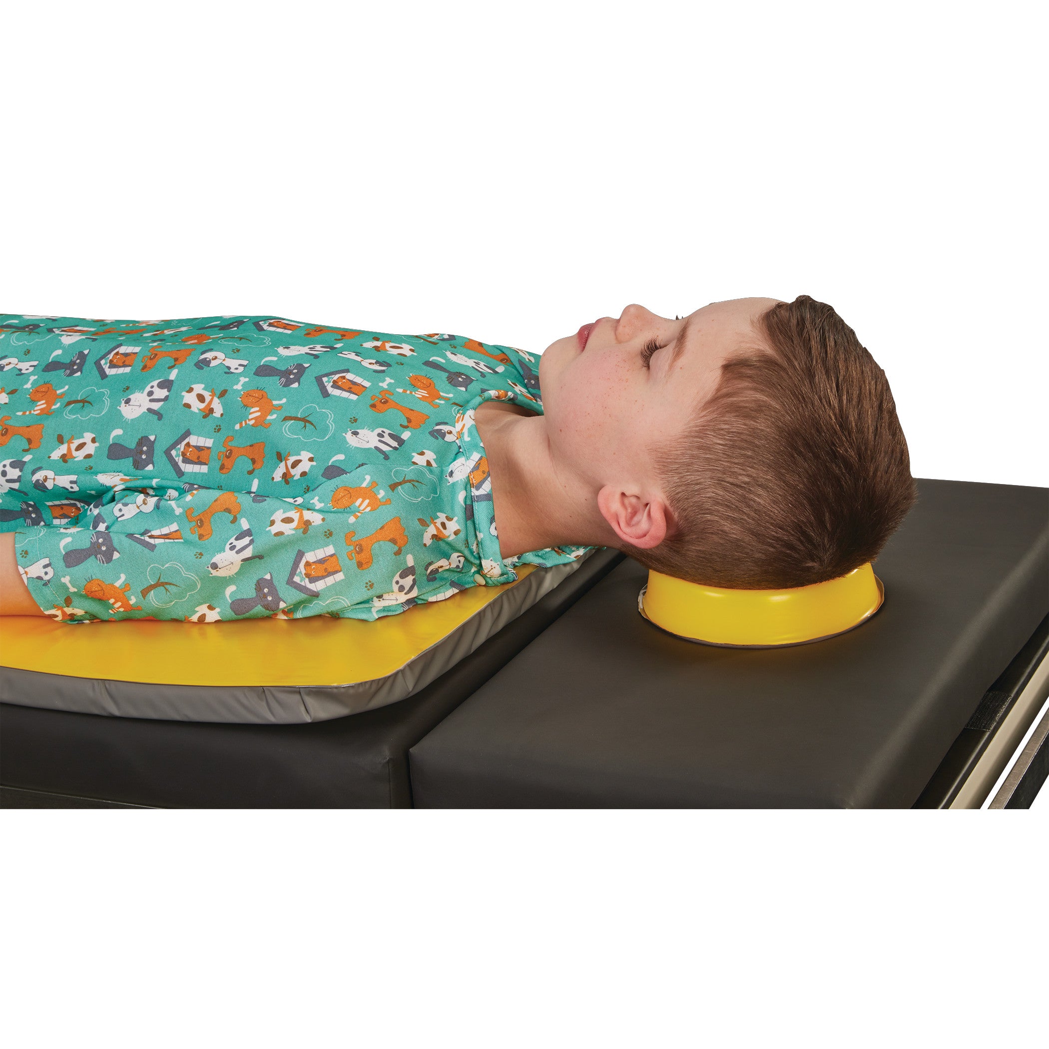 A child lies with their head on an AliMed AliLite Head Donut, a yellow head support, while wearing a printed teal gown.