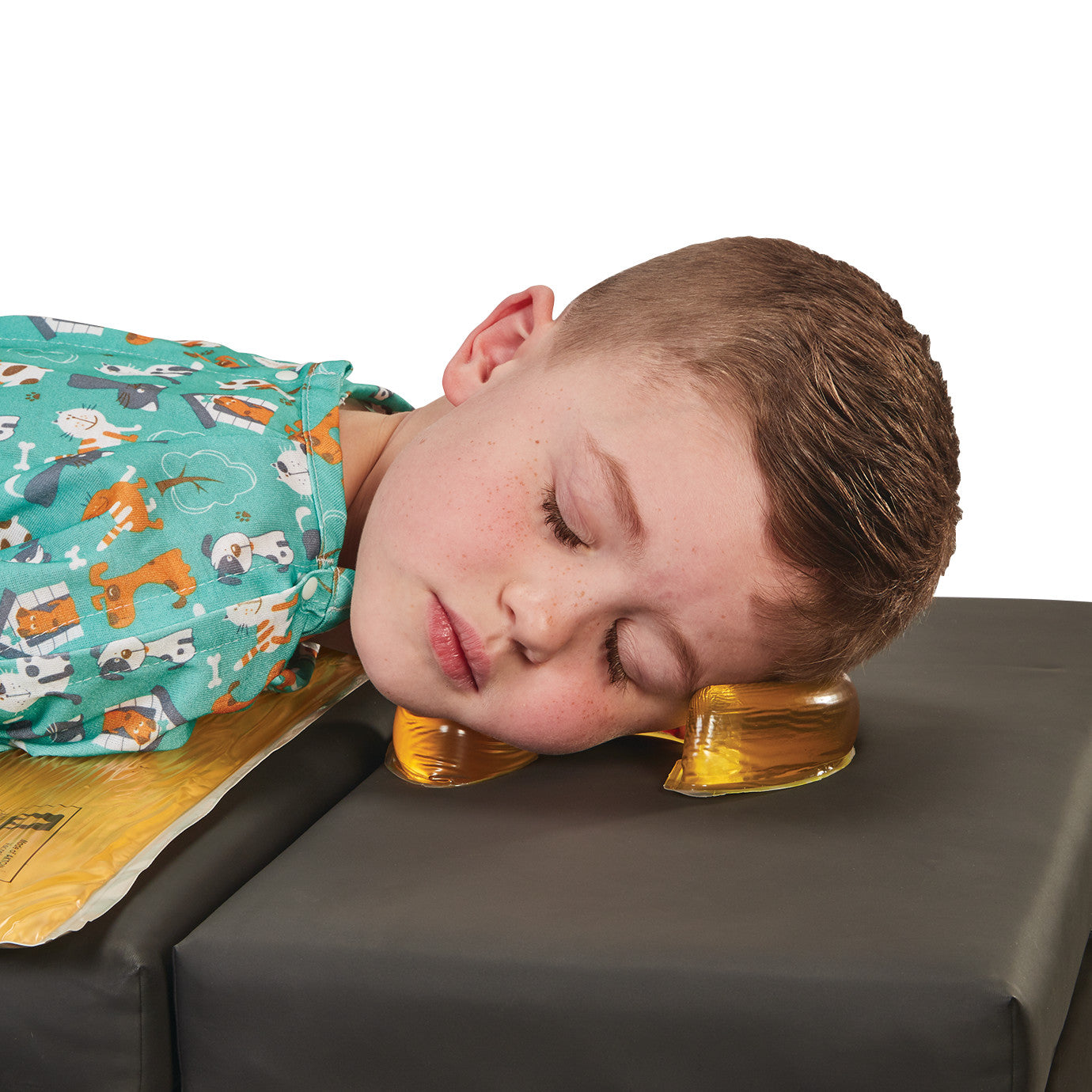 A child resting their head on the AliMed AliGel Horseshoe Donut pillow while lying on a cushioned surface, eyes closed.