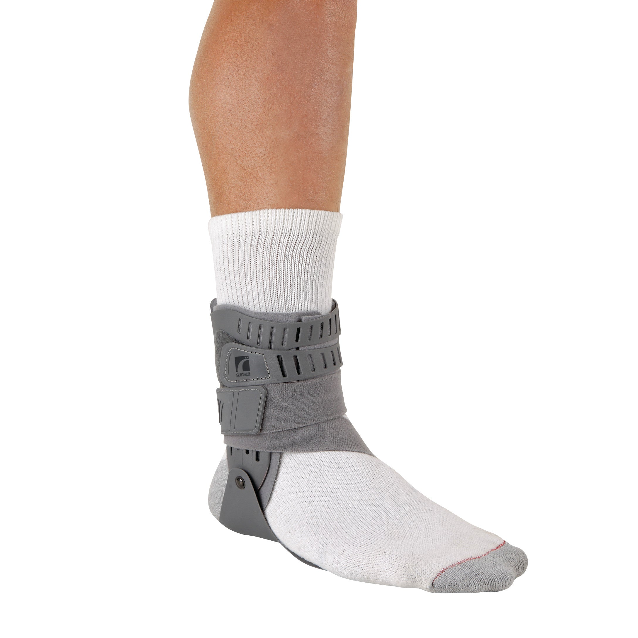 A person wearing an Ossur Rebound Ankle Brace over a white sock. The brace is gray and supports the ankle.